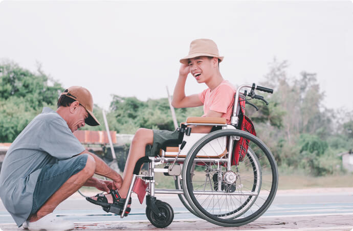 A boy in a wheelchair being assisted with his father in a wheelchair